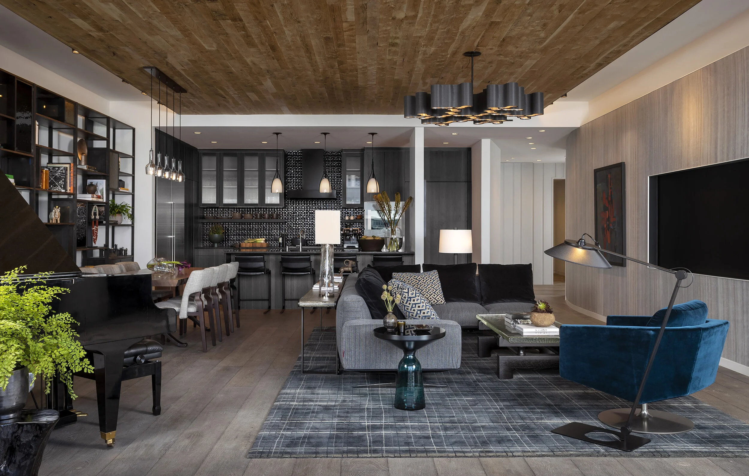 Grand piano with lush green plant, open-plan living, modern black kitchen, wood plank ceiling