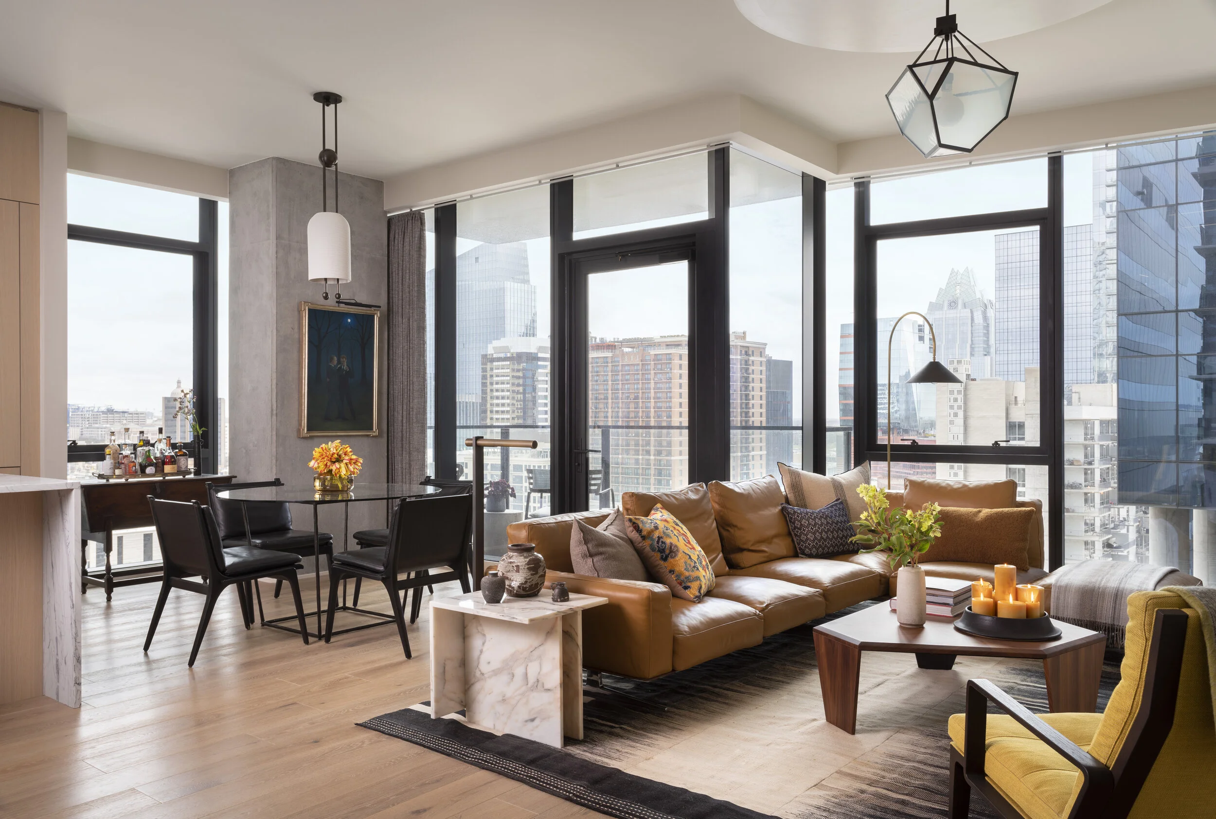 Panoramic skyline views through floor-to-ceiling windows, caramel sofa, yellow accent chair, marble table
